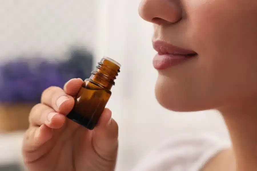 A woman smelling essential oil and wondering, “Can you put essential oils on your skin?